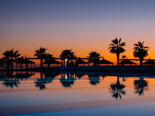 Obraz premium Sunset with silhuettes palm and reflection in swimming pool 