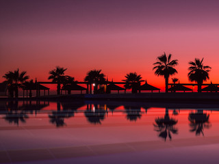 Sunset with silhuettes palm and reflection in swimming pool	