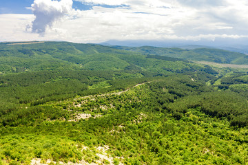 View of the beautiful hilly valley, bird's-eye view, covered with a variety of forests and shrubs, is among the mountains of the Crimean Peninsula. On which there is a picturesque road. Wild natural u