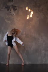 Beautiful slim young female modern jazz contemporary style ballet dancer wearing a black leotard and white shirt on a loft studio background