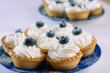 Tartlets filled with curd cream and decorated with blueberries on top are on a blue plate on a light (white) background, close up