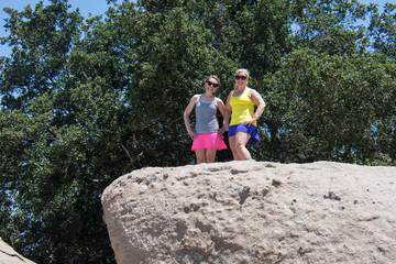 Naklejka na ściany i meble Two adult women hikers stand on the top of a giant boulder, happy, in the sunshine