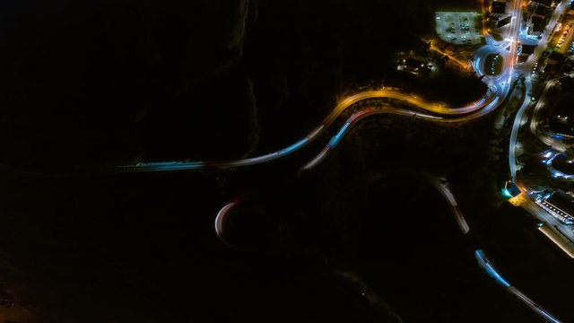 Timelapse of elevated view cars driving on beautiful S curved road in mountains at night, Nago, Italy. Aerial Dronelapse of hillside roads through forest with turns at evening. Long exposure shots.