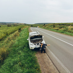 man sitting on road near broken car. trying stop car for help