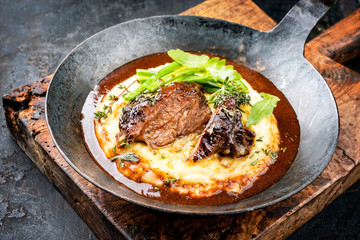 Traditional German braised veal cheeks in brown sauce with mashed potatoes and beans as closeup in a wrought-iron pan
