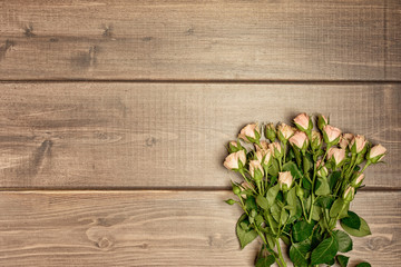 On the table of natural wooden planks, lies a bouquet of small spray roses. Copy space. Spring layout.