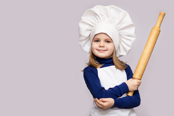 Children cook. Happy little girl in chef uniform holds rolling pin isolated on white background