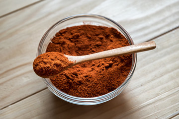 Paprika Powder on wooden spoon, in a glass bowl jar on a wooden table