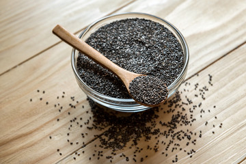 Raw organic black chia seeds on wooden spoon, in a glass bowl jar on a wooden table