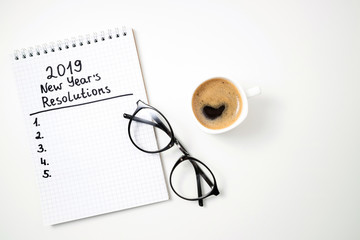 New year resolution 2019 on desk. 2019 goals list with notebook, coffee cup and glasses on white background. Goal, plan, strategy, change, idea concept. Top view and copy space
