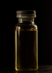 small medical Bottle, with yellow inside, on a black background, close-up,