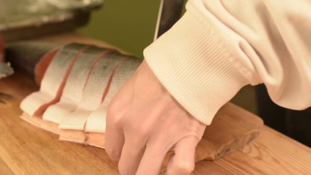 Close-up of female hands are cutting with a knife a large salmon on a wooden table of home cooking