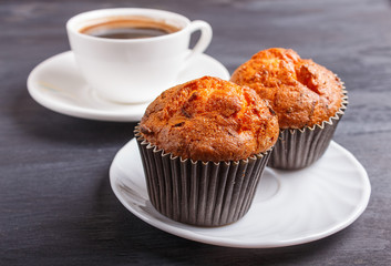two carrot muffins with cup of coffee on white plate on black wooden background