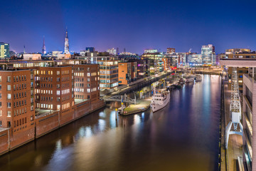 The Harbor District (HafenCity) in Hamburg, Germany, at night. Panoramic aerial view of the Sandtorkai and the Kaiserkai across the traditional port Sandtorhafen.