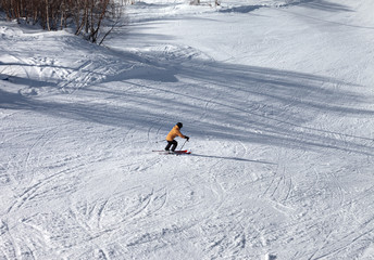 Skier descents on snowy ski slope at sun winter day