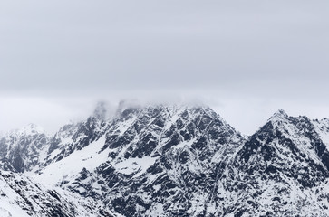 Rocky mountains in snow and overcast grey sky at winter