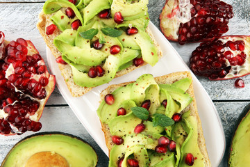 sliced avocado and ripe pomegranates on toast bread with spices and avocado.