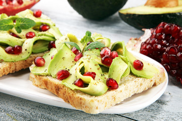 sliced avocado and ripe pomegranates on toast bread with spices and avocado.