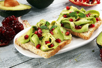 sliced avocado and ripe pomegranates on toast bread with spices and avocado.
