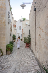 giovane ragazza vestita di bianco cammina per le strade di matera in una via con delle piante ai lati della strada
