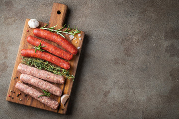 Assorted fresh sausages with thyme, rosemary, olive oil and garlic on a wooden chopping Board on a...