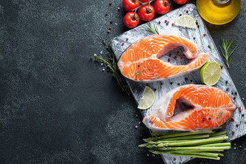 Two raw fresh salmon or trout steaks, rich in omega-3 oil, with lime, thyme and olive oil on a dark background. Healthy and dietary food. Top view with copy space. Flat lay