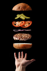 fly burger with beef sliced tomatoes pickles and onion on black. floating food levitating burger