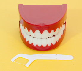 It's never too late for conscientious dental care. Dental floss and fake teeth on a yellow background. Fun. Humor.
