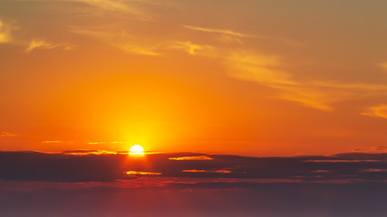 sky during a colorful, bright orange sunset, sun's rays make their way through the clouds