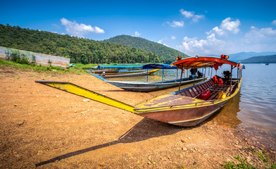 Many long trail boats are parked at the river side, with the island behind in Thailand. Selection focus only on some points in the image