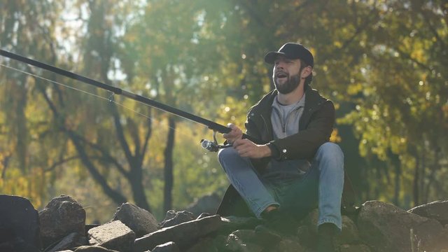 Excited fisherman spinning fishing reel, caught fish, pulling rod, happiness