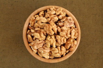 Big shelled walnuts in bamboo bowl on rough green tarpaulin cloth