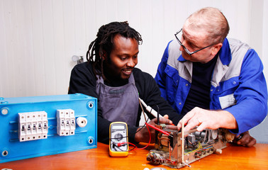 An experienced teacher teaching a young Electrician in the Workshop