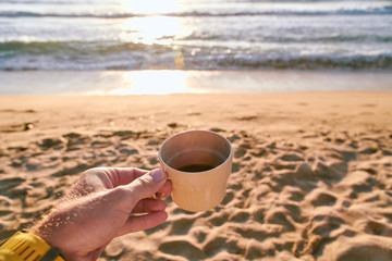 Fototapeta na wymiar Hand with coffee on a sandy beach during susnet in Corsica