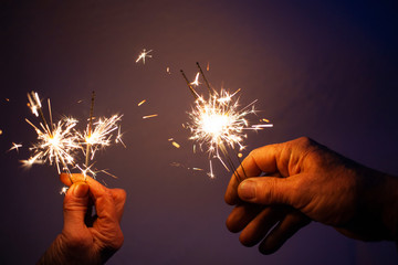 hands of elderly couple holding sparkles celebrating New Year