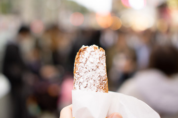 Tourist’s hand holding snack while walking in crowded street (day time)