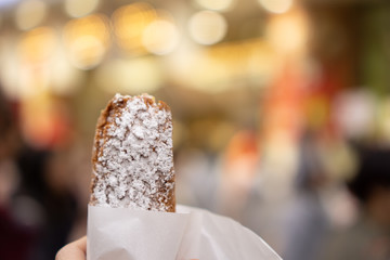 Tourist’s hand holding snack while walking in crowded street (day time)