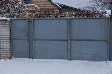 gray metal closed gate and part of the fence on the street in white snow