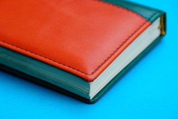 red green notepad with leather cover lying on a blue desk