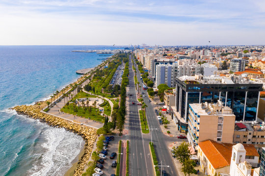 Aerial view of Molos Promenade park on coast of Limassol city centre,Cyprus. Bird's eye view of the beachfront walk path and palm trees, Mediterranean sea, piers, urban skyline and port from above