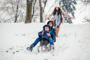 Young mom chasing her cute sons while they are sledding