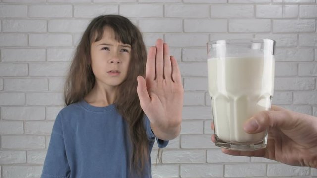 Child rejecting glass of milk. Lactose intolerance. Little girl shows no gesture to a glass of milk.