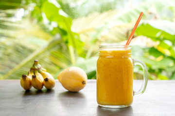 Smoothie with tropical fruits: mango, banana, pineapple in a glass jar on the wooden table. The concept of a healthy lifestyle. Close up