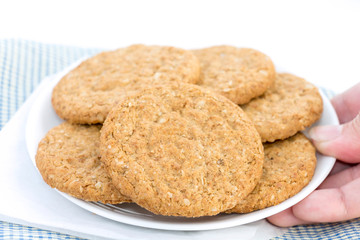 Woman hand holding homemade shortbread cookies made of oatmeal pile in plate on blue cloth background. Concept food healthy snack for enjoy in holiday. with copy space for text.