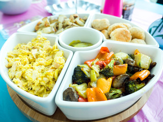 The top view of a white ceramic appetizer tray filled with mixed fried  vegetables, Jamaican dumplings and ackee and saltfish, fried potatoes, and pickle slices in the center for a gender reveal party