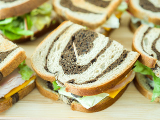 Close up of several simple appetizer sandwiches for a party using marbled rye bread with orange cheddar cheese, lettuce, apple slices, turkey meat and honey mustard on wood bamboo cutting board.