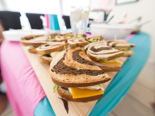 Close up of several simple appetizer sandwiches for a gender reveal party using marbled rye bread with orange cheddar cheese, lettuce, apple slices, turkey meat and honey mustard on wood cutting board