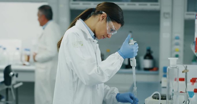 Portrait of female scientist with a pipette analyzes a liquid to extract the DNA and molecules in the test tubes in laboratory. Shot in 8K. Concept: research,biochemistry, pharmaceutical medicine