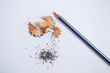 A pencil sharpened with pencil peels and black graphite lead waste on a white background