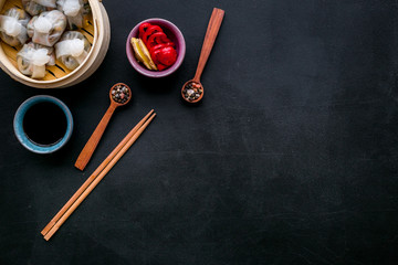 Dim sums with red pepper and vegetables with sticks and black tea in Chinese restaurant on black background top view mockup